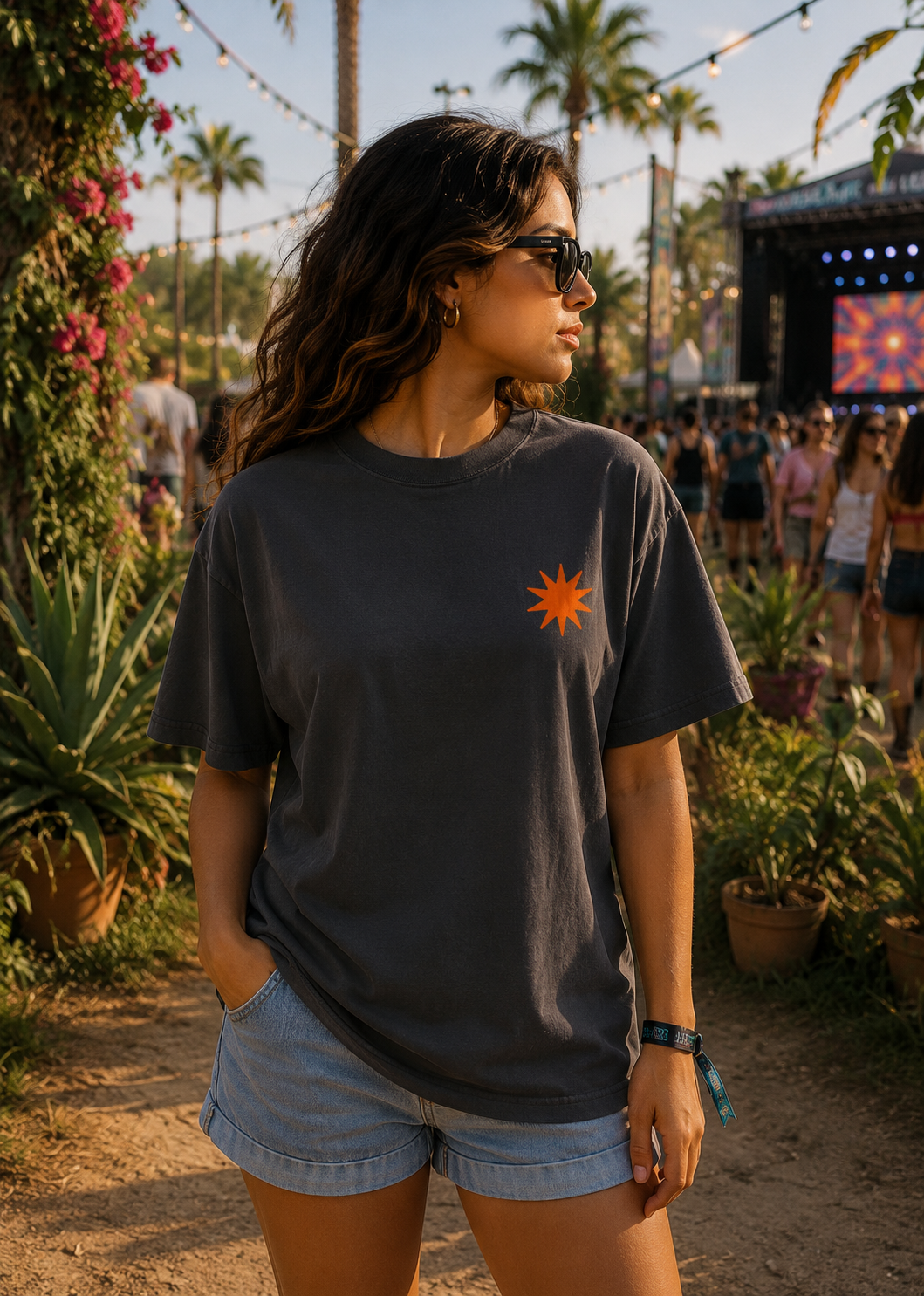 Woman wearing a dark gray t-shirt with a sun graphic at an outdoor event with palm trees and stage lights.